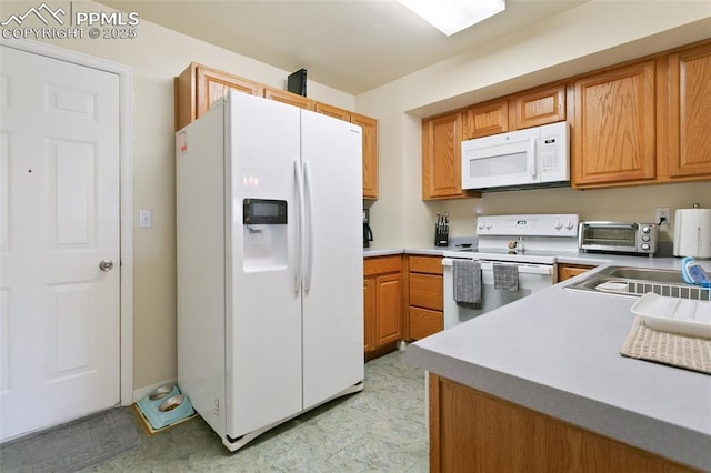 kitchen with white appliances, light countertops, and brown cabinetry