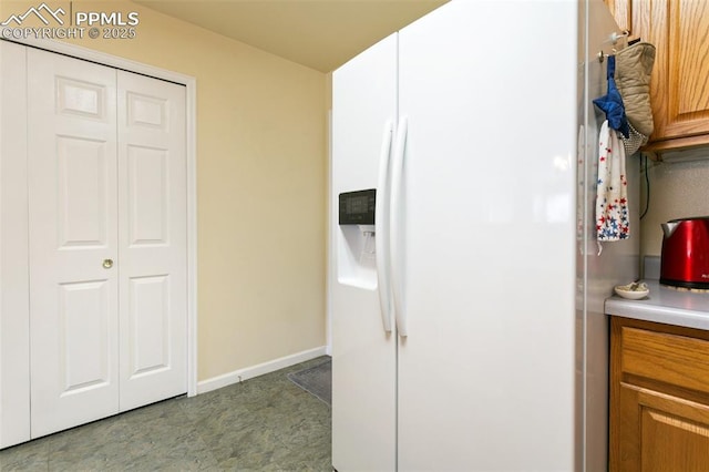 kitchen with white fridge with ice dispenser, baseboards, light countertops, and brown cabinetry