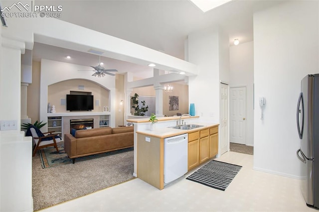 kitchen with white dishwasher, freestanding refrigerator, a sink, light brown cabinets, and a glass covered fireplace