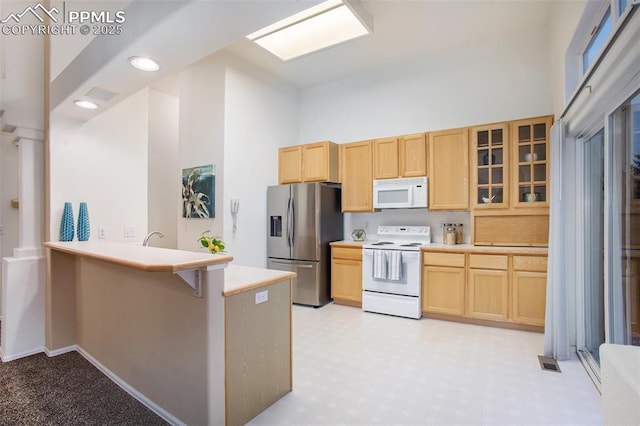 kitchen with white appliances, light brown cabinets, glass insert cabinets, a peninsula, and a high ceiling