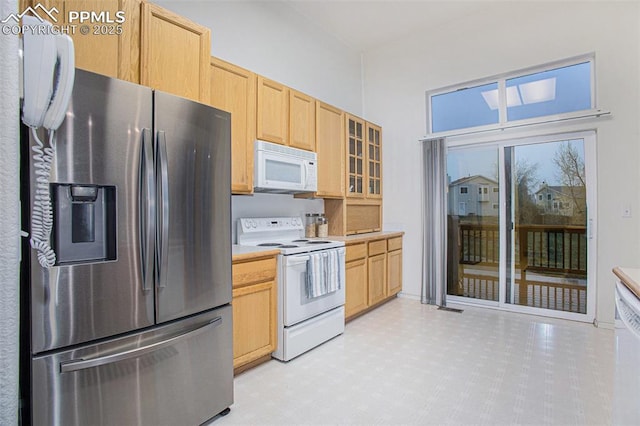 kitchen featuring white appliances, light brown cabinetry, light countertops, light floors, and glass insert cabinets
