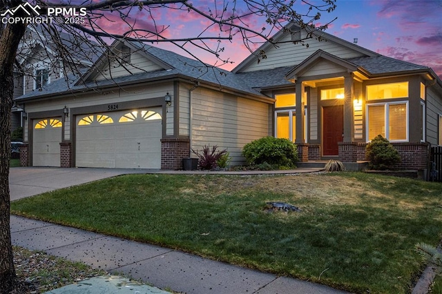 craftsman house with brick siding, a lawn, an attached garage, concrete driveway, and roof with shingles