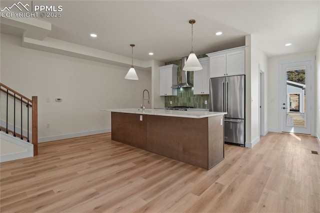 kitchen with high quality fridge, wall chimney range hood, backsplash, light countertops, and light wood-type flooring