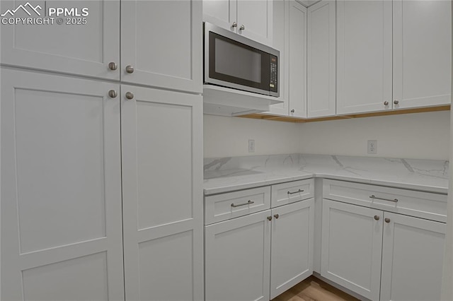 kitchen featuring stainless steel microwave, white cabinets, and light stone counters