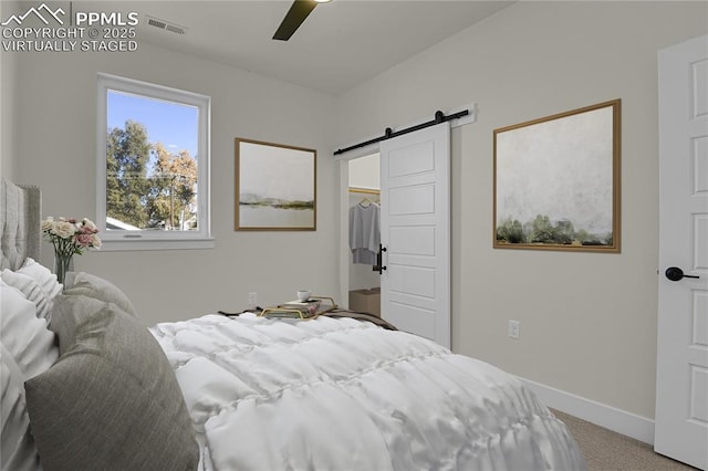 carpeted bedroom featuring a barn door, baseboards, a walk in closet, and a ceiling fan