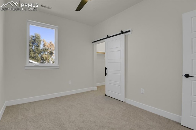 unfurnished bedroom with a barn door, light carpet, and baseboards