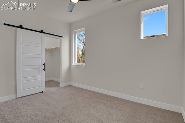 unfurnished bedroom featuring a barn door, light carpet, baseboards, and a ceiling fan