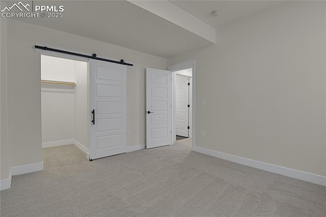 unfurnished bedroom with carpet, a barn door, baseboards, a spacious closet, and a closet