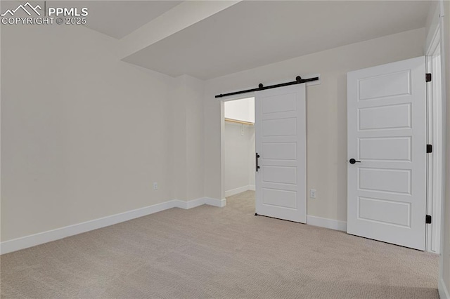 unfurnished bedroom featuring a barn door, light colored carpet, baseboards, and a spacious closet