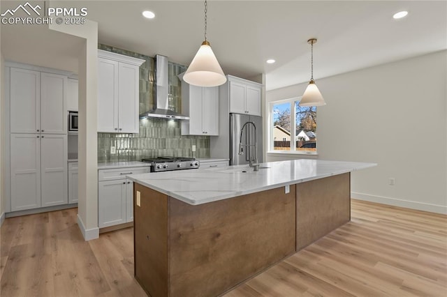 kitchen with wall chimney exhaust hood, a sink, an island with sink, white cabinetry, and light wood-type flooring