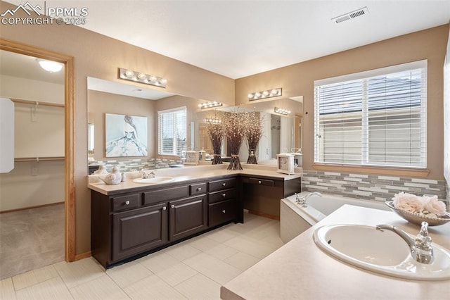 11985 Hanging Valley Way, Colorado Springs, CO 80921 - full bathroom featuring two vanities, decorative backsplash, a spacious closet, and a bathtub