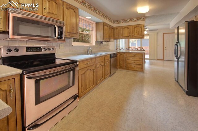 770 Allegheny Dr, Colorado Springs, CO 80919 - kitchen with appliances with stainless steel finishes, brown cabinetry, light countertops, tasteful backsplash, and a peninsula