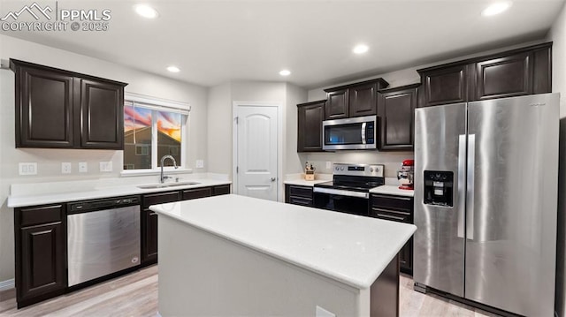 kitchen featuring a center island, a sink, appliances with stainless steel finishes, light countertops, and light wood-style floors