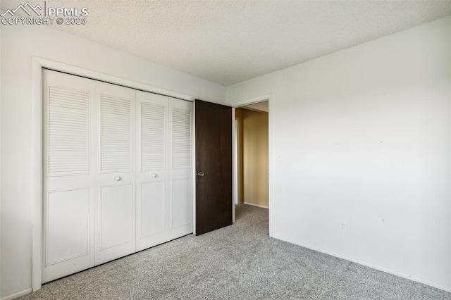unfurnished bedroom featuring light carpet, a closet, a textured ceiling, and baseboards