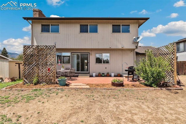 rear view of house with a chimney, a patio, and fence