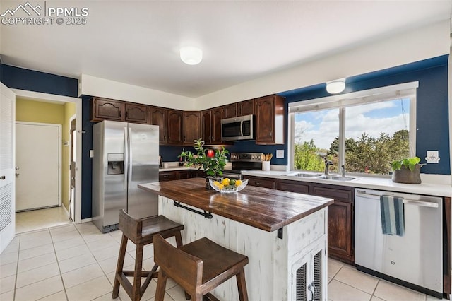 kitchen with appliances with stainless steel finishes, a sink, wooden counters, dark brown cabinetry, and light tile patterned floors