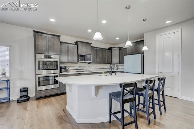 kitchen featuring appliances with stainless steel finishes, a sink, dark brown cabinets, light wood-style floors, and light countertops