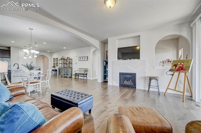 living area featuring arched walkways, a chandelier, baseboards, recessed lighting, and light wood finished floors
