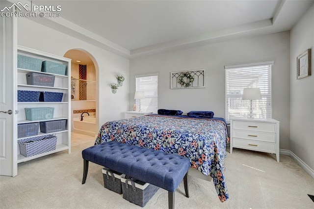 carpeted bedroom with arched walkways, connected bathroom, and baseboards