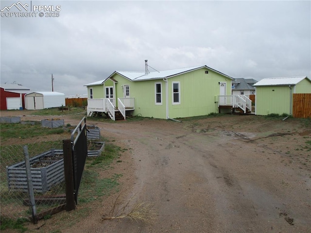 view of front of property featuring a storage unit, a garden, an outbuilding, a deck, and dirt driveway