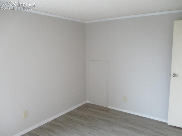 spare room with crown molding, wood finished floors, and baseboards