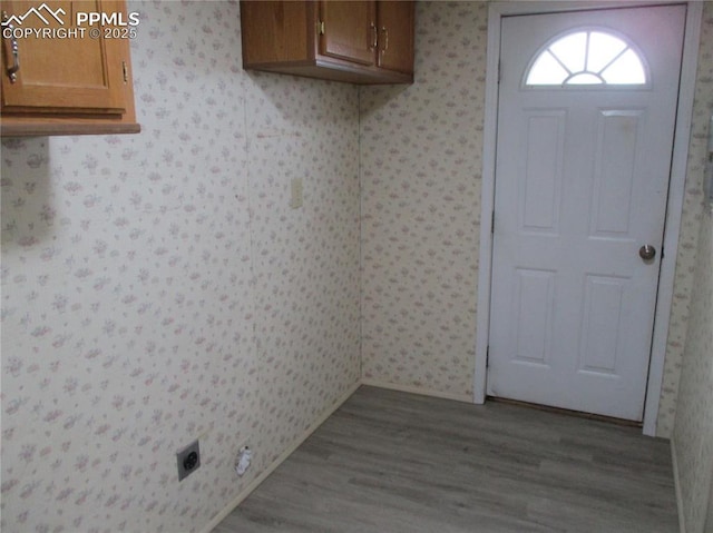 washroom with cabinet space, wallpapered walls, wood finished floors, and electric dryer hookup
