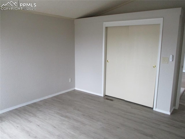 unfurnished bedroom featuring wood finished floors, baseboards, a closet, and lofted ceiling