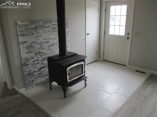 doorway to outside featuring a wood stove, baseboards, and light wood-style floors