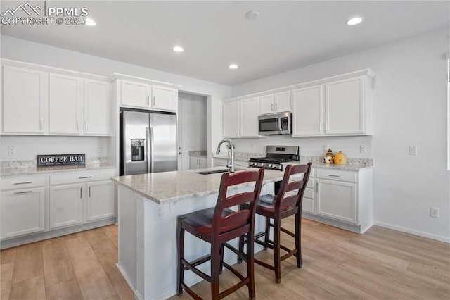 16422 Mountain Flax Dr, Monument, CO 80132 - kitchen with appliances with stainless steel finishes, light wood-style floors, white cabinets, a kitchen island with sink, and recessed lighting