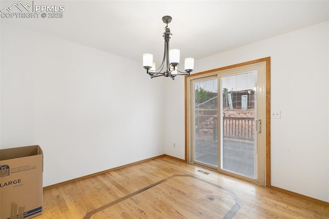 unfurnished dining area featuring a chandelier, light wood-type flooring, and baseboards