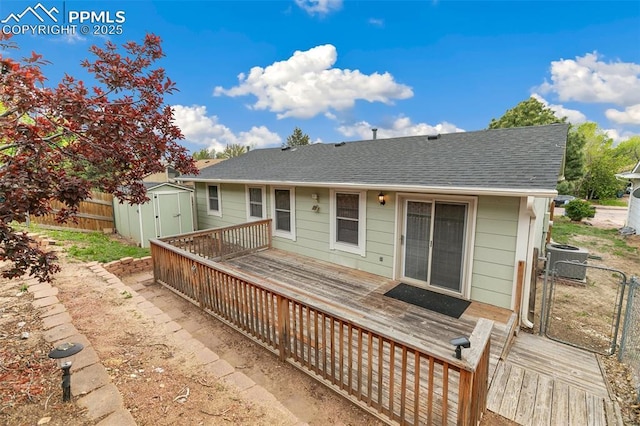 back of house with central AC unit, a storage unit, a deck, and a shingled roof