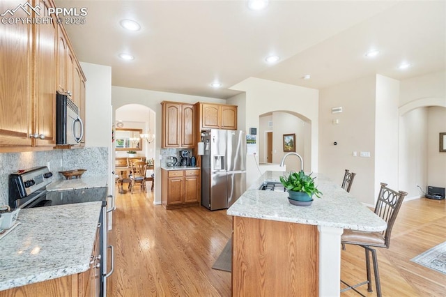 kitchen featuring appliances with stainless steel finishes, arched walkways, a kitchen bar, tasteful backsplash, and light wood finished floors