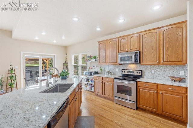 kitchen with stainless steel appliances, a sink, light stone countertops, light wood-style flooring, and backsplash