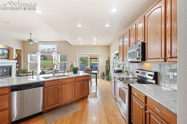 kitchen with appliances with stainless steel finishes, a sink, light wood-type flooring, light stone counters, and ceiling fan