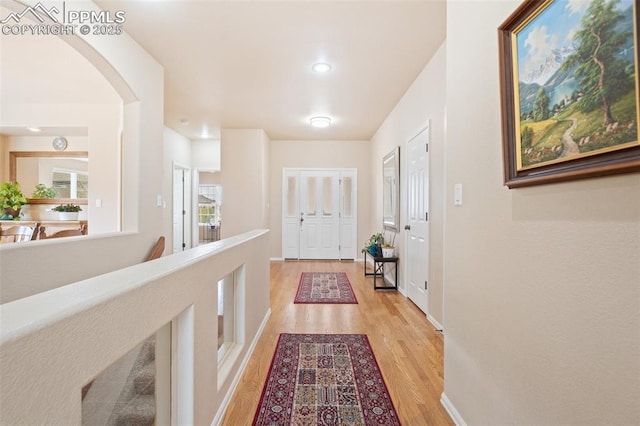 hall featuring light wood-style floors, arched walkways, baseboards, and recessed lighting