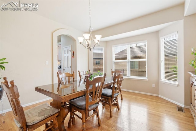 dining space with a chandelier, arched walkways, light wood finished floors, and baseboards