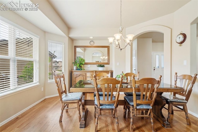 dining space with a chandelier, baseboards, arched walkways, and light wood-style flooring