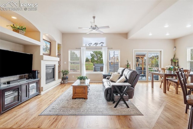 living room featuring a ceiling fan, a glass covered fireplace, light wood finished floors, recessed lighting, and baseboards
