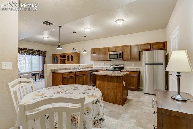 7567 Black Spruce Hts, Colorado Springs, CO 80908 - kitchen with appliances with stainless steel finishes, a kitchen island, a peninsula, brown cabinets, and decorative light fixtures