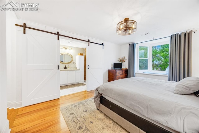 313 E Evans Ave, Pueblo, CO 81004 - bedroom with a barn door, light wood-style floors, a sink, and ensuite bath