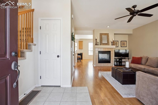 entryway featuring ceiling fan, a tiled fireplace, light wood finished floors, baseboards, and stairs