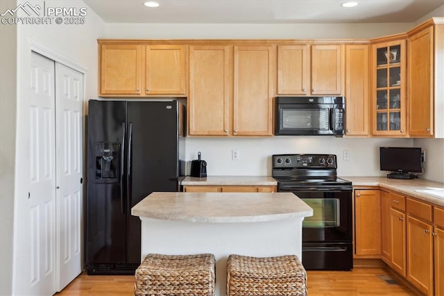 kitchen featuring black appliances, recessed lighting, light countertops, glass insert cabinets, and light wood finished floors