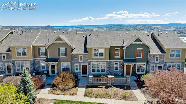 view of front of home featuring stone siding, a mountain view, and a shingled roof
