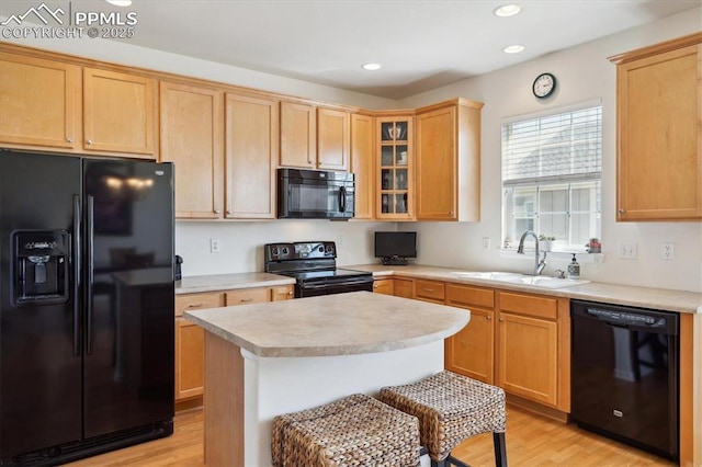 kitchen with black appliances, a sink, light countertops, light wood-style flooring, and glass insert cabinets