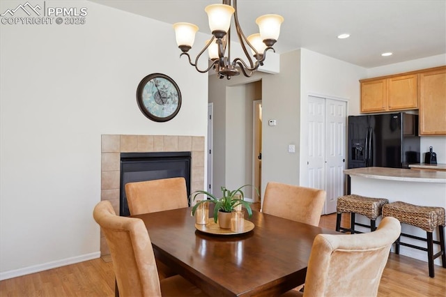 dining area with light wood-style flooring, a chandelier, recessed lighting, a tiled fireplace, and baseboards