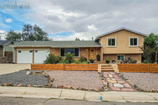 tri-level home featuring a garage, concrete driveway, brick siding, and fence