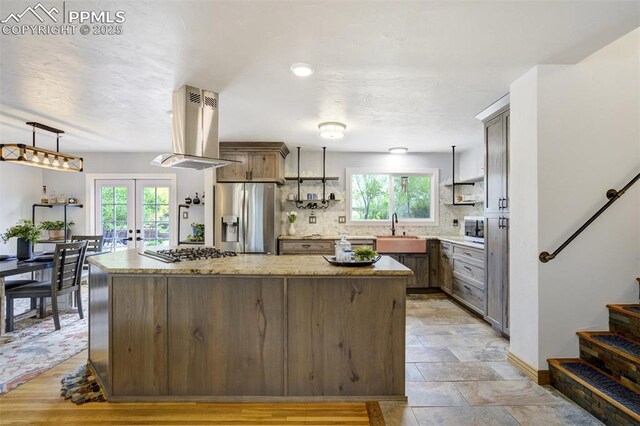 kitchen featuring stainless steel appliances, island range hood, a sink, a center island, and french doors