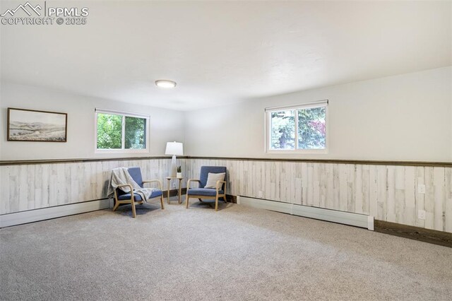 sitting room with a baseboard heating unit, carpet floors, plenty of natural light, wainscoting, and wooden walls