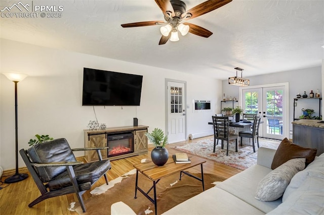 living area featuring french doors, a ceiling fan, a glass covered fireplace, and light wood finished floors