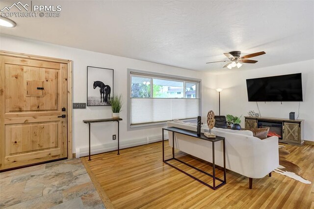 living area featuring light wood-style flooring, ceiling fan, and baseboards
